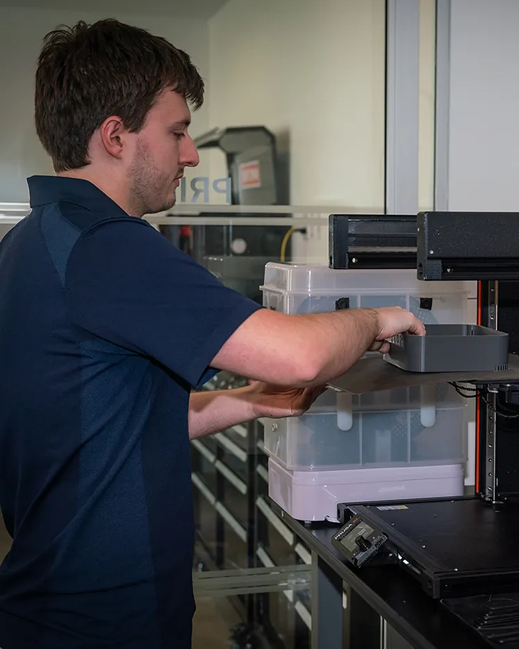 An engineer loading a freshly printed enclosure into a 3D printer in the lab