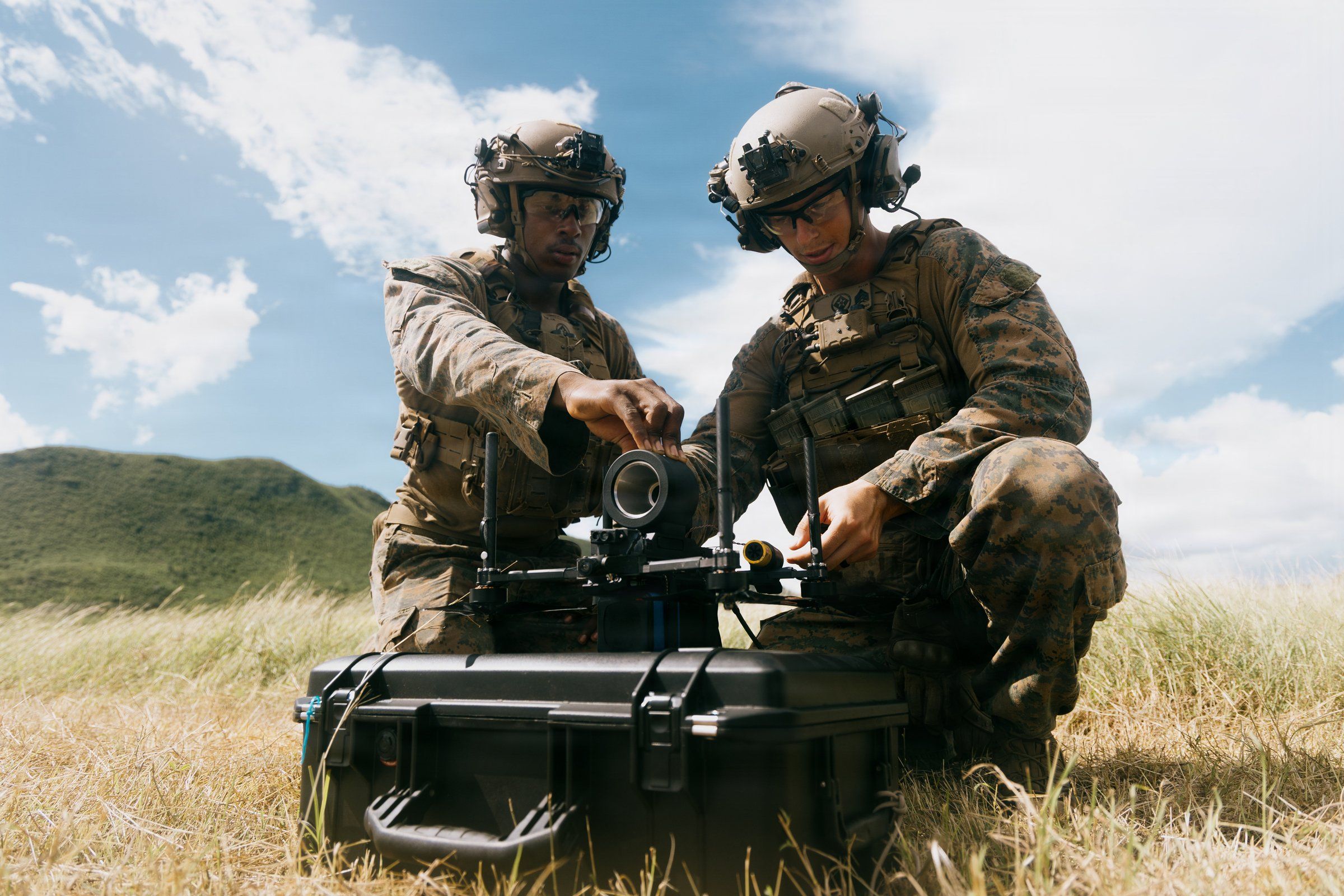 Two Marines working with field equipment in a grassy landscape